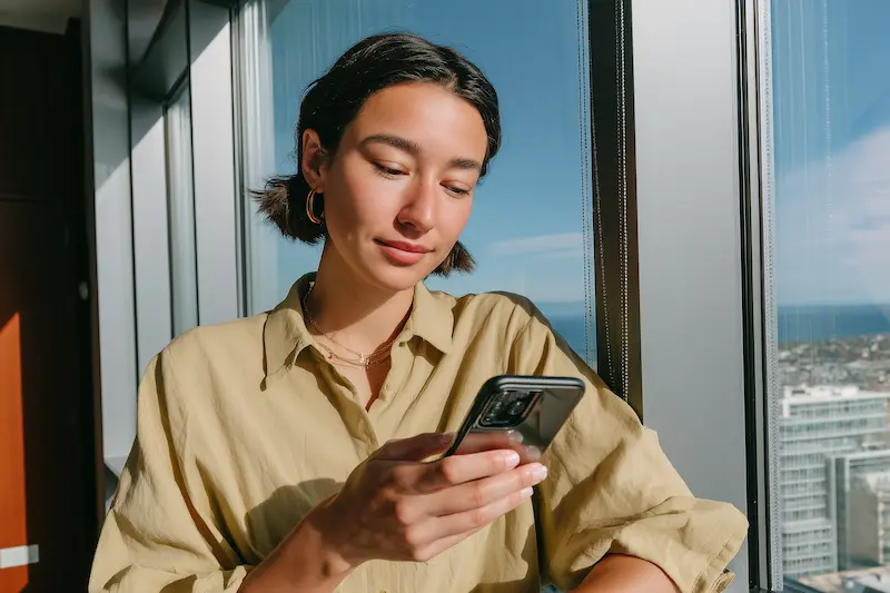 Woman Looking at Her Phone by a Window. What Is Psychological Counseling?